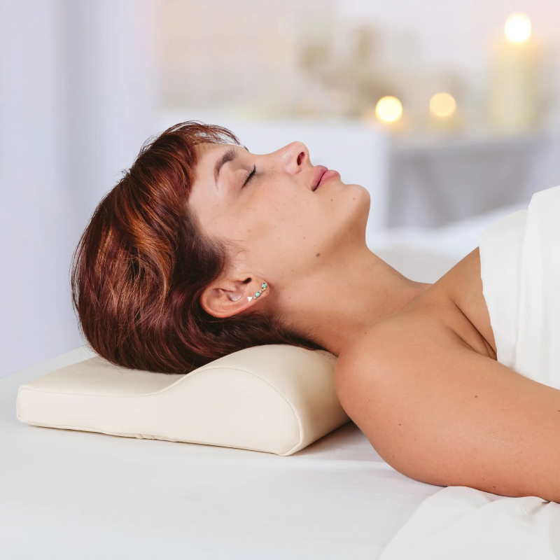 Earthlite Neck Contour Bolster massage pillow shown in use, under the head on a massage table.